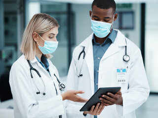 Healthcare, covid and doctors checking tablet for medical data, patient chart or insurance documents in hospital lobby. Face mask, man and woman working in medicine consulting internet before surgery