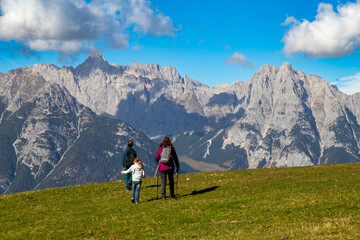 Fototapeta na wymiar Wandern mit Kindern in Seefeld, Tirol: Familie wandert über eine Almwiese, im Hintergrund das Wettersteingebirge