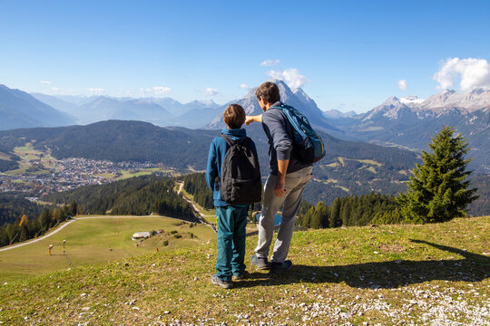 Wandern mit Kindern in Seefeld, Tirol: Vater zeigt seinem Sohn die Landschaft. Der schneebedeckte Gipfel am rechten Bildrand ist die Zugspitze