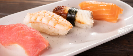 Nigiri sushi with salmon, eel, tuna and prawn, served on white plate. Delicious traditional Japanese food, tasty seafood, restaurant menu, food background