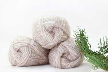 Gray woolen skeins of warm yarn on a white background with a spruce branch. Vertical. Knitting, hobby. Copy space