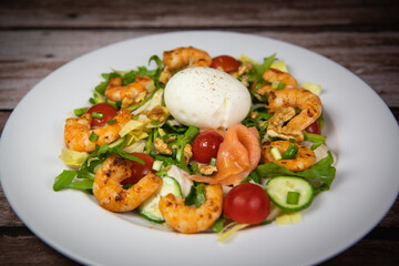 Recipe for rocket salad, endive, tomato, cucumber, soft-boiled egg, fried shrimp with paprika, smoked salmon and nuts. High quality photo