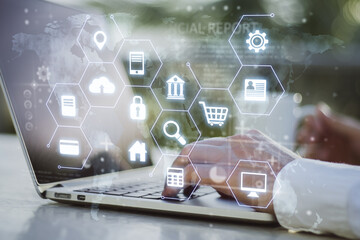 Close up of man hands using laptop computer on office desktop and abstract glowing digital icons hologram on blurry background. Digital transformation and technology concept. Double exposure.