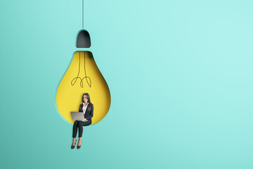 businesswoman sitting on abstract hanging light bulb chair and using laptop on blue background with mock up place. Idea, innovation, work culture and inspiration concept.