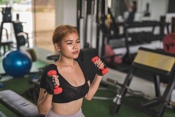 A young and sexy asian woman does seated dumbbell hammer curls on a flat bench at the gym. Wearing...
