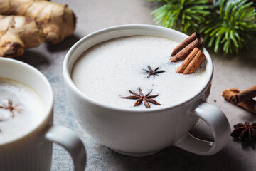 Homemade chai latte with cinnamon and star anise in white cup, dark background.