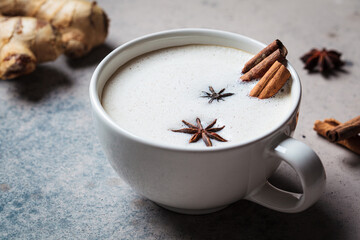 Homemade chai latte with cinnamon and star anise in white cup, dark background.