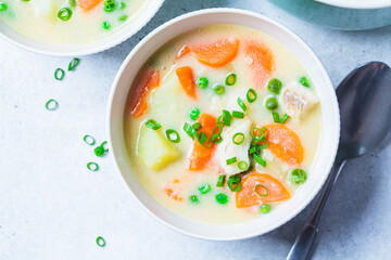 Fish cod chowder soup with green peas, potatoes and carrots in white bowl.