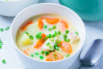 Fish cod chowder soup with green peas, potatoes and carrots in white bowl.