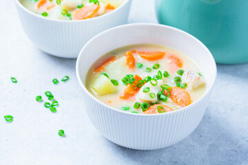Fish cod chowder soup with green peas, potatoes and carrots in white bowl.