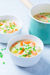 Fish cod chowder soup with green peas, potatoes and carrots in white bowl.