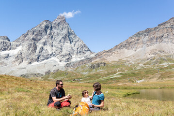 Fototapeta premium Couple with her little girl having a picnic close to a lake under the Matterhorn at italian alps.