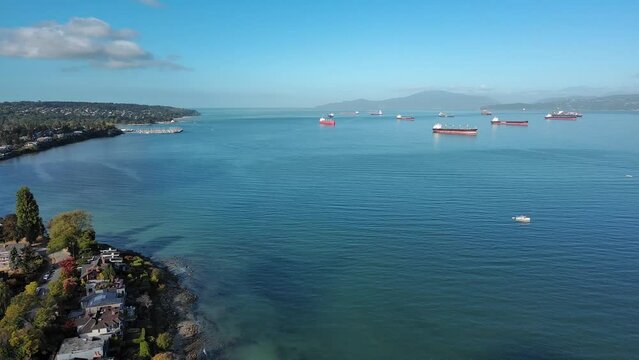Drone shot of Kitsilano in Vancouver, British Columbia showing residential homes, condo apartment, beach, ocean, ships mountains and trees.