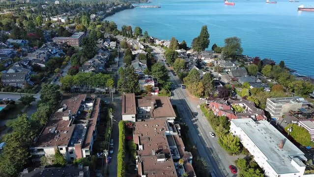 Drone shot of Kitsilano in Vancouver, British Columbia showing residential homes, condo apartment, beach, city skyline, cars on streets, ocean, ships and trees.