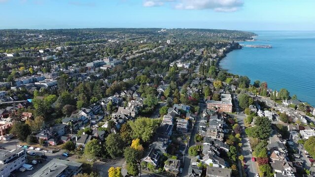 Drone shot of Kitsilano in Vancouver, British Columbia showing residential homes, condo apartment, beach, city skyline, cars on streets, ocean, ships and trees.