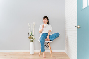 椅子に座ってホットドリンク・コーヒー・お茶を飲むアジア人女性
