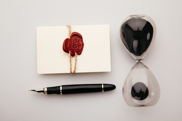 Paper envelope with wax seal stamp, pen and hourglass on a table. Top view