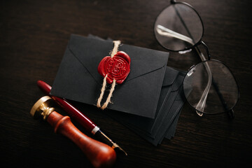 Black envelope with red wax seal, stamp and glasses on a dark table