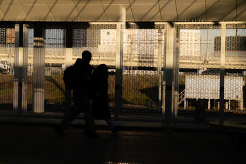 Naklejka na ściany i meble Male and female silhouettes in the shadows and without faces walk through the train station. Copy space