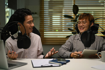 Happy male radio hosts using condenser microphone, recording voice over radio interview guest conversation at studio