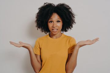 Confused doubtful black woman shrugging with shoulders, feeling baffled while looking at camera