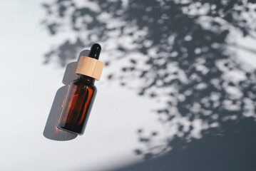 Amber bottle with cannabis oil used for medical purposes. White background with daylight and flowers shadows. Soothing cbd oil. Alternative Medicine