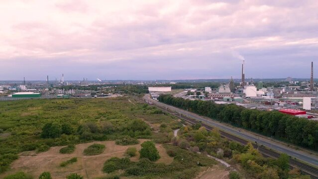 Fast flying drone towards an passenger tram on tracks to S&uuml;rth, Cologne, Germany - aerial bird view of an chemical industry plant in the background and a little forest green zone in the front 2022