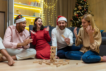 New year party, various friends at home on floor playing game, men and women smiling and happy...