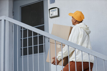 Fototapeta na wymiar Back view of delivery worker going up stairs to house door with package, copy space