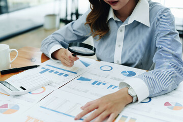 Financial analysts analyzing business financial reports are examining documents using a magnifying glass as a working concept