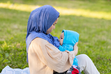 breast feeding concept. young islamic woman hugging newborn baby boy in park. asian mother in hijab...