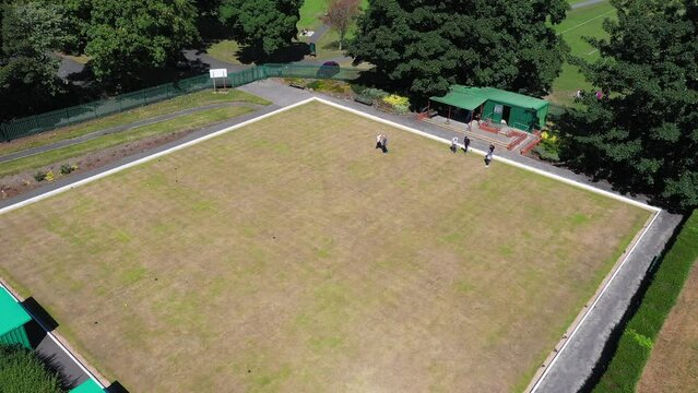 Aerial drone footage of a British Bowling green with people playing Bowls on the public park in the summer time, filmed in the city of Leeds in West Yorkshire in the UK on a sunny day in the summer.