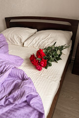 A bouquet of red roses lies on the white-lilac bed linen. Aesthetic minimalism. Greeting card with good morning