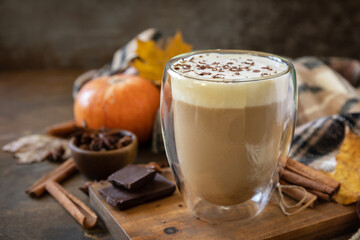Pumpkin latte spice coffee, warm scarf and maple leaves on rustic background. Seasonal autumn...
