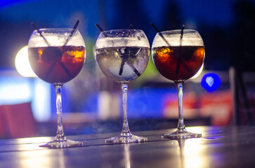 Beautiful row line of different colored alcohol cocktails on a party, martini, vodka,and others on decorated catering bouquet table on open air event, picture with beautiful bokeh