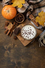 Obraz na płótnie Canvas Seasonal autumn concept with hot drink. Pumpkin latte spice coffee, warm scarf and maple leaves on rustic background, creative flat lay. View from above. Copy space.