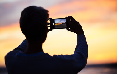 Man silhouette, smartphone and beach sunset photograph for social media post. Young photographer...