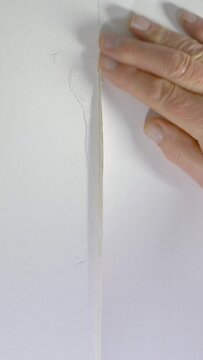 Vertical video social media format &ndash; Closeup of a man&rsquo;s hands using a small brush and paste to glue back two sections of wallpaper which have come apart, then pressing the repair area into place.