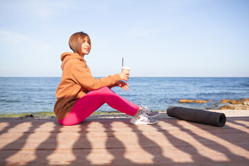A beautiful woman leads a healthy lifestyle, practises yoga in nature. The girl is wearing a pink fuchia tracksuit and does streching exercises on the street against the background of sea