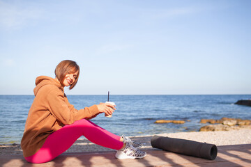 Fototapeta na wymiar A beautiful woman leads a healthy lifestyle, practises yoga in nature. The girl is wearing a pink fuchia tracksuit and does streching exercises on the street against the background of sea