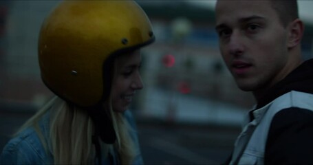 A young stylish couple of bikers meet and hug near a motorcycle standing in a public city parking lot.