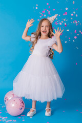 girl in a beautiful dress and a cardboard hat stands on a blue background and throws confetti