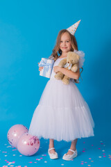 girl in a beautiful fluffy white dress holds a teddy bear and a gift box in her hands