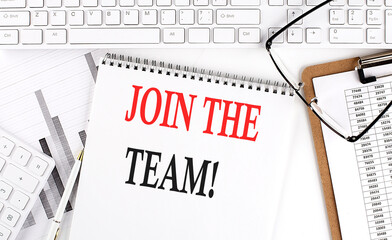 Text JOIN THE TEAM on Office desk table with keyboard, notepad and analysis chart on white background.