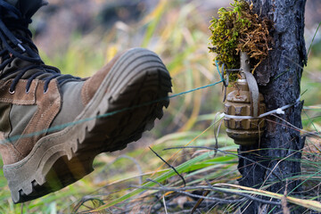 Close-up photo - a soldier steps on a mine trap. The soldier's boot rips off the wire and rips off the pin of the grenade.