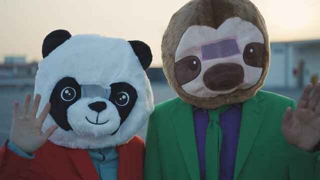 Cinematic video of a couple wearing elegant suits and funny animals masks having fun and celebrating outdoor in a a parking lot rooftop