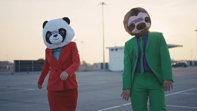 Cinematic video of a couple wearing elegant suits and funny animals masks having fun and celebrating outdoor in a a parking lot rooftop