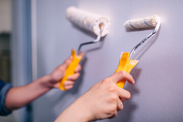 close-up of hands using foam rollers applying white paint to the walls.
