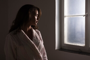 Young woman in bathrobe suffering from cancer standing beside hospital window