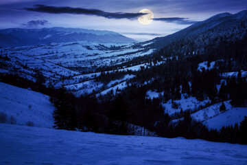 carpathian rural landscape in winter at night. snow covered hills in full moon light. scenery with krasna ridge in the distance. synevir village in the valley